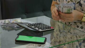 mulher mãos estão segurando uma dólar conta e uma calculadora e telefone estão em a escrivaninha. video