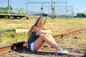 Sad young girl sitting lonely on rail track photo