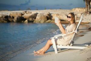 Woman with pad relaxing in chaise-lounge on the beach photo