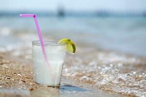 Glass of lemonade or water on beach by sea photo
