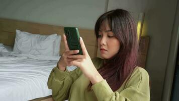 Asian woman sitting in her room while scrolling on her phone video