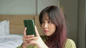 Asian woman sitting in her room while scrolling on her phone video