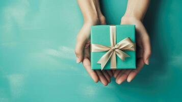 Top view of hands holding gift box with copy space on turquoise background, Ai Generative. photo