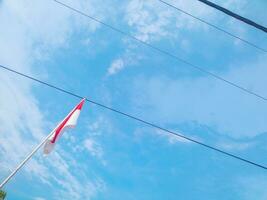 red and white flag of Indonesia against the sky and power lines in the background photo