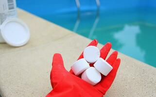 blanco pequeño cloro tableta en el mano de un rojo protector guante de un piscina desinfección Servicio obrero. el comenzando de el nadando temporada en el caliente verano en vacaciones. foto
