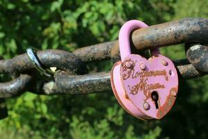 rosado amor candado adjunto a cadena. oxidado bloquear con corazón forma tallado colgando al aire libre. san valentin día, unidad, memoria conceptos foto