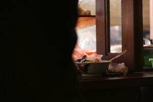 un indonesio hombre calle comida vendedor sirve un cliente. un mujer preparando un plato llamado 'pollo fideos' a clientes en el calle foto