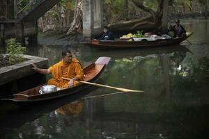 Ratchaburi Tailandia - 11 de enero de 2019 - tailandés monje navegación madera barco en estrecho canal en dumneón Saduak distrito en Ratchaburi para recibiendo comida en temprano Mañana foto