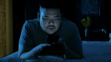 an asian man relaxing on the bed in bedroom and using mobile smart phone while laydown. video