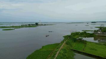 a Titas river with a boat in it, boat is in the middle of a river, group of people on a boat in a body of water. A small island with a tower in the middle of the water. A person fishing in the water. video