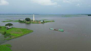 the boat is traveling through a flooded area, boat is in the water near a Brick making chimney, a chimney in the middle of a the river, vast expanse of water, with a small island in the middle video