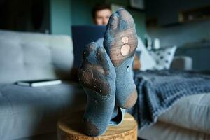 Man with leaky socks resting on sofa, using laptop photo