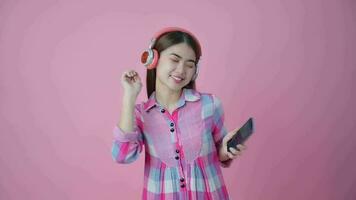 Asian cute young woman wearing headphones and listening to music on mobile phone happy dancing pose video