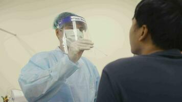 médico enfermero médico trabajador en un protector uniforme hace pcr prueba a asiático hombre enfermo paciente, el étnico afro chico da un saliva análisis apertura boca y sonriente, el coronavirus epidemia video