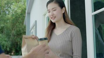 Happy smiling Asian woman receives paper box parcel of food from courier front house. Delivery man send deliver express. online shopping, paper container, takeaway, postman, delivery service, packages video