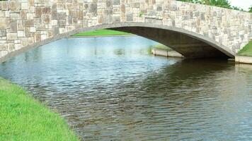ein klein Brücke gemacht von Granatwerfer und Fliesen Kreuze ein Golf Kurs Teich mit Grün Gras. video
