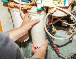 Women's hands remove flasks with contaminated water purification filters to be replaced with clean ones. The process of replacing the cartridges of a multi-stage water filter. photo