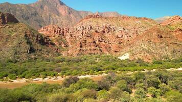 aéreo ver zumbido volador terminado escénico rojo rocoso montañas y rojo río con un claro azul cielo. video