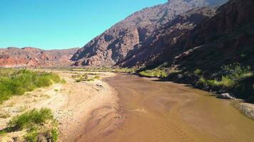 antenn se Drönare flygande över naturskön röd klippig bergen och en röd flod landskap med en klar blå himmel. quebrada de las conchas, cafayate, salta, argentina. video