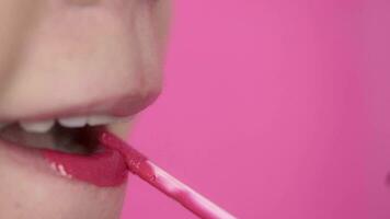 Close up of a woman applying pink lipstick on pink background. video