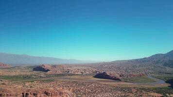 aéreo ver zumbido volador terminado escénico rojo rocoso montañas y árido Desierto paisaje con un claro azul cielo. video