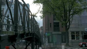 visie van klein plastic figuur van ik ben AMSTERDAM brieven beeldhouwwerk Aan de brug tegen wazig stadsgezicht, Amsterdam, Nederland video