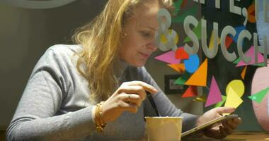 mujer en café comiendo helado y utilizando almohadilla video
