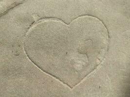 A heart is engraved in a big natural stone. The sign for love in a huge rock in the middle of a forest. Trees and green leaves in the background. A carved symbol in a block. photo