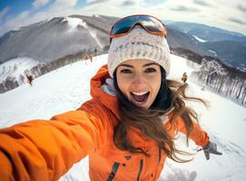 A woman wearing an orange jacket is selfieing on a snowy slope photo