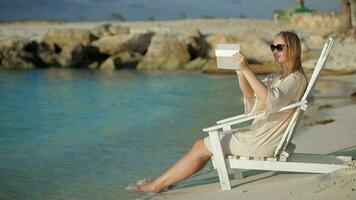 Woman with pad making photos of sea sitting in the deck chair on beach video