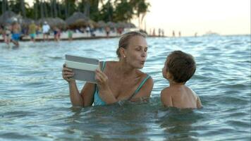 madre con almohadilla haciendo foto o vídeo de hijo en agua video