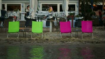 Four empty chaise-lounges on the beach with cafe behind video