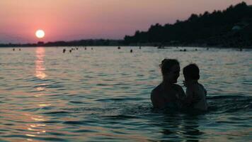 Mother throwing son in sea at sunset video