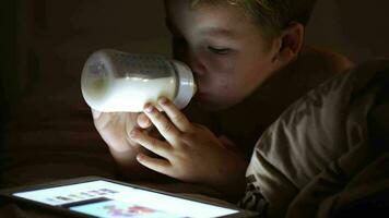 Boy drinking milk from the bottle and looking at touchpad video