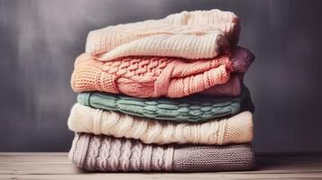 Bunch of knitted warm pastel color sweaters with different knitting patterns folded in stack on brown wooden table, grunged texture wall background. Generative AI photo