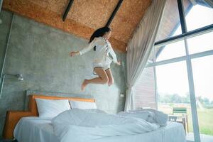 attractive asian woman jumping on bed in the morning, in the morning, She felt very refreshed, natural window light. photo