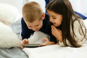 People, children, technology, friends and friendship concept - happy little girls boy with smartphones lying on floor at home photo