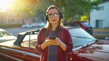 vrouw is staand buitenshuis in de buurt de rood wijnoogst auto en gebruik makend van smartphone video