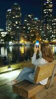 Woman takes pictures of the skyscrapers of Vancouver on her smartphone at night video