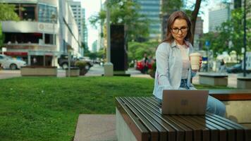 zorgeloos bedrijf vrouw zit buitenshuis met koffie en gebruik makend van laptop, afgelegen werk video