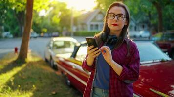 mulher é em pé ao ar livre perto a vermelho vintage carro e usando Smartphone video