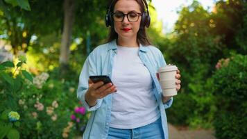 donna con caffè e smartphone a piedi attraverso il fioritura giardino video