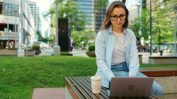 zorgeloos bedrijf vrouw zit buitenshuis met koffie en gebruik makend van laptop, afgelegen werk video