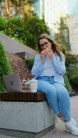 Woman having a lunch with a sandwich and coffee in the park with a laptop video