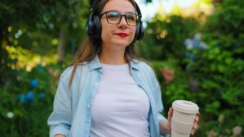 Woman with coffee and smartphone walking through the blooming garden video