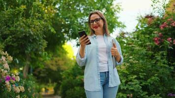 mujer con ordenador portátil y teléfono inteligente caminando mediante el floreciente jardín video