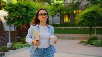 Woman walking on street with laptop and coffee in hands after work day video