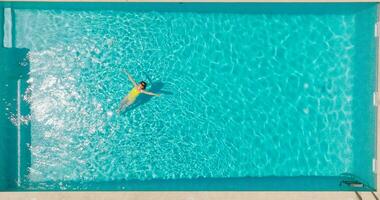 parte superior abajo ver de un mujer en amarillo traje de baño acostado en su espalda en el piscina. video