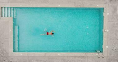 parte superior abajo ver de un hombre en rojo pantalones cortos nada en el piscina. video