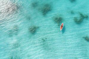 aéreo ver de un kayac en el turquesa mar, aéreo ver de un mujer en un tabla de surf en el turquesa aguas de el Maldivas, ai generado foto